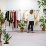 Woman browsing clothes in a boutique surrounded by indoor plants and stylish displays. Ideal fashion retail scene.